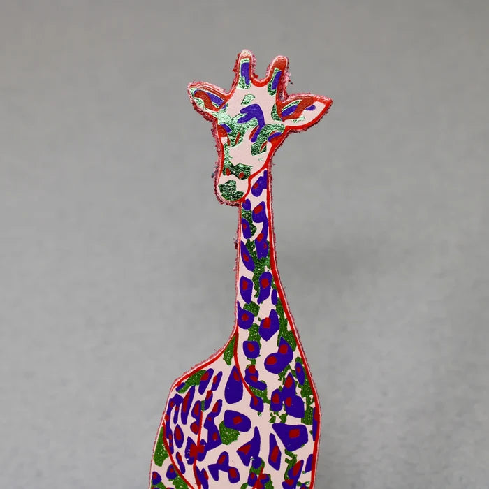 Colorful giraffe bookmark in pale pink, purple, and metallic green on a gray background