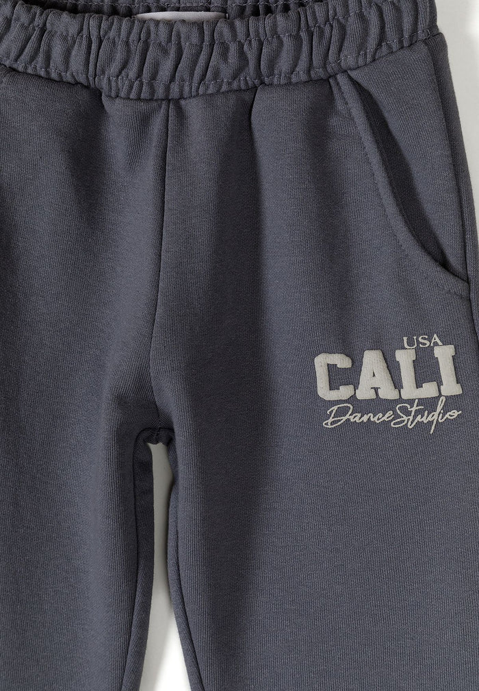 Detail of grey tapered jogging trousers with elasticated waistband and logo.