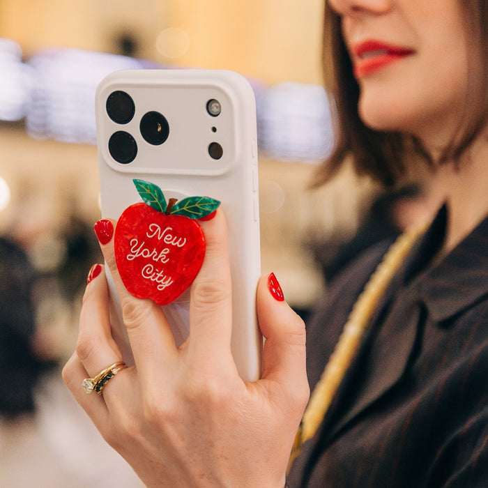 Person holding a phone with an apple-shaped 'New York City' phone holder, blurred background