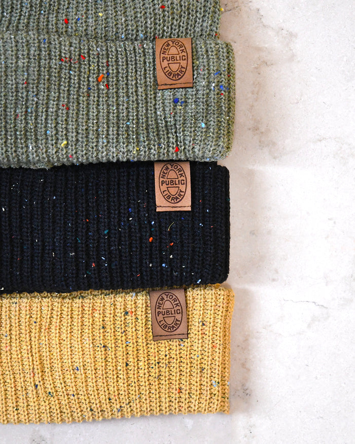 Three knit beanie hats in green, black, and yellow with visible brand labels on a light marble background.