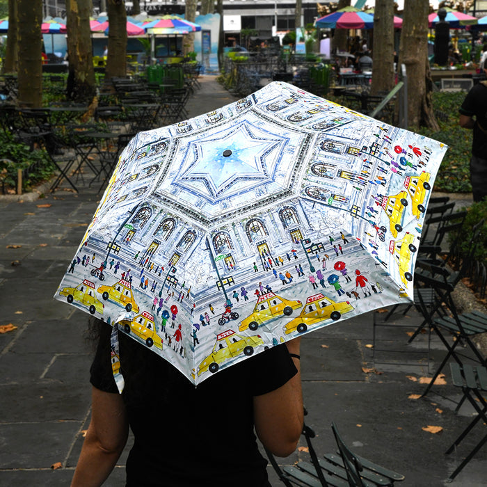 Person holding a colorful umbrella featuring an illustration of NYPL's flagship building during the winter season in an urban park setting
