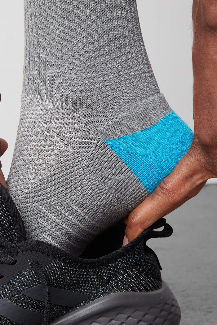 Side view of a man putting on a shoe and wearing AIRKNITx Crew Sock in Grey Heather
