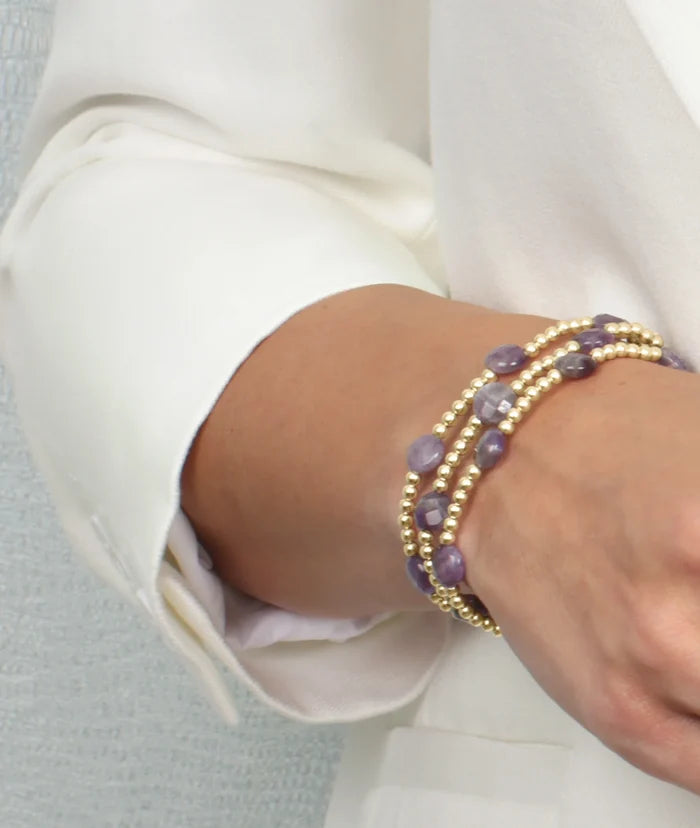 Close up photo of model's wrist with three gold bead stackable bracelets with 8 millimeter faceted gemstones between every six 3 millimeter beads.