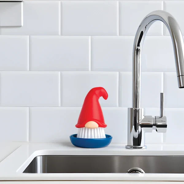 Kitchen sink with gnome-shaped dish brush & drainer and faucet in a tiled kitchen.