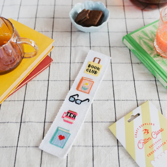 Cross-stitched bookmark with various symbols on a table.