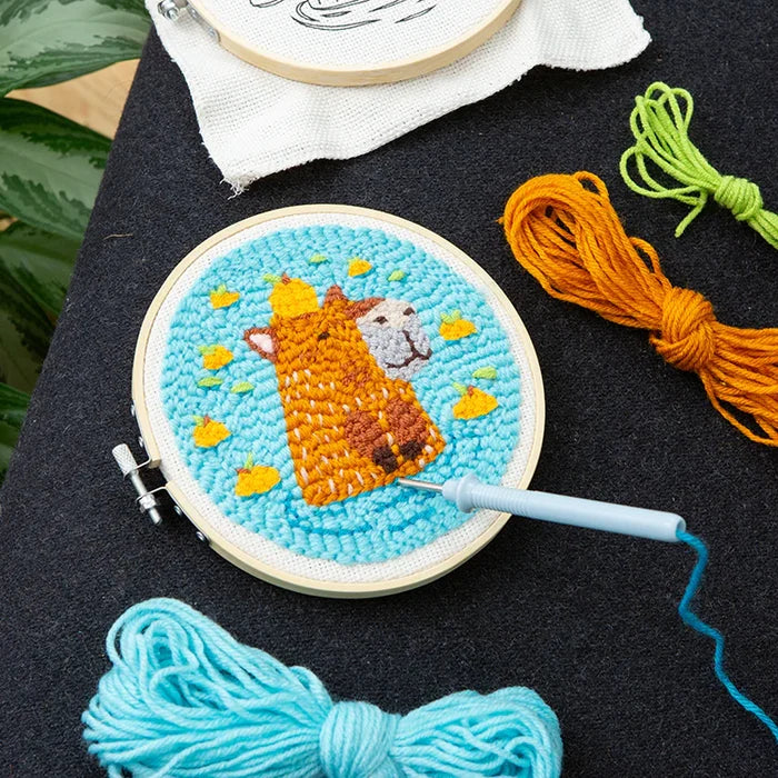 Embroidery hoop with a completed design of capybara surrounded by yarn and an embroidery hoop.