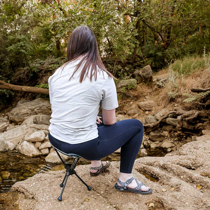 Person sitting on a portable stool by a stream in a forest