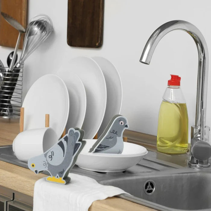 Two sponges with pigeon design on a kitchen counter next to a sink.