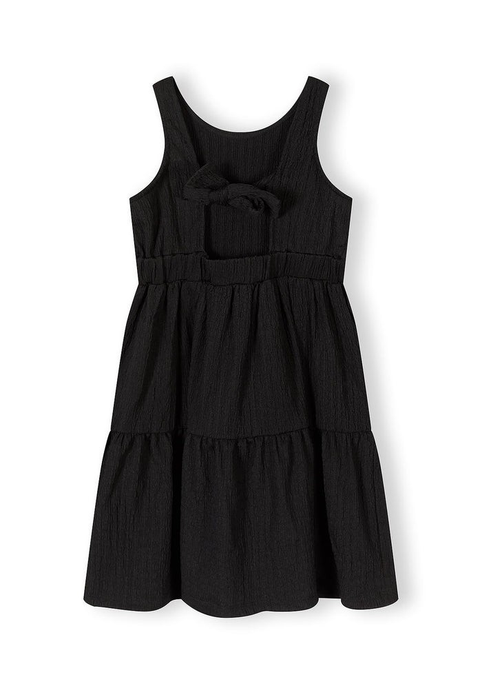 Girls tiered sleeveless black summer dress, front view with bow detail.