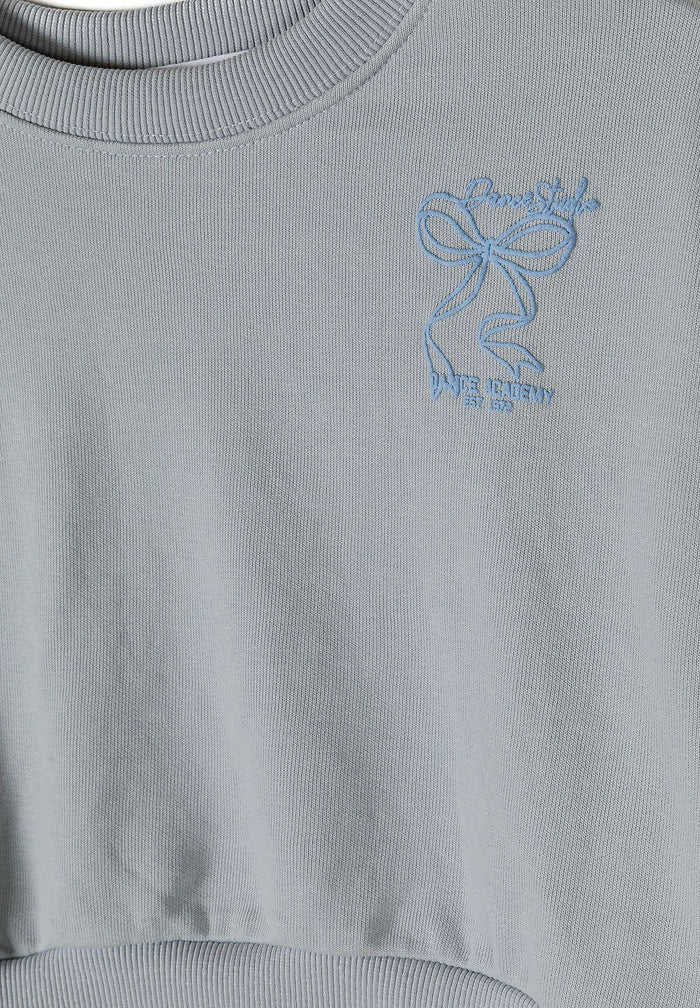 Detail of a light blue girls' tracksuit with a logo embroidery.