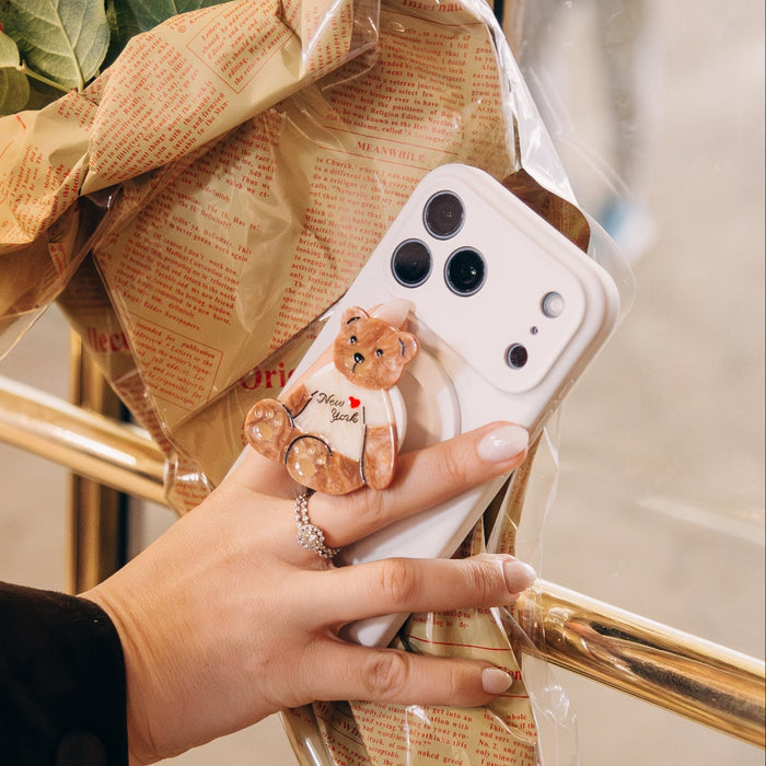 Bouquet of red roses wrapped in brown paper with a phone case featuring a bear design held by a hand.