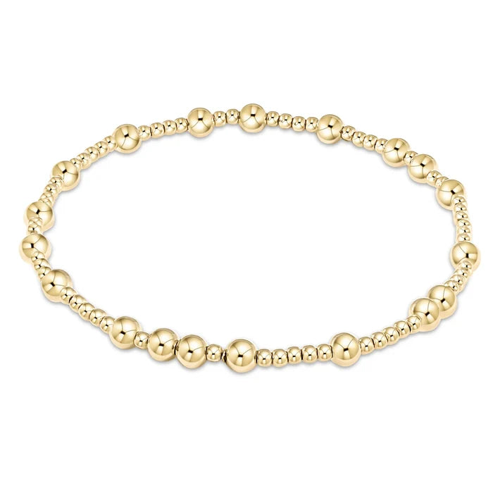 Gold bead stackable bracelet with an asymmetrical design featuring a combination of 3 millimeter beads and 6 millimeter beads.