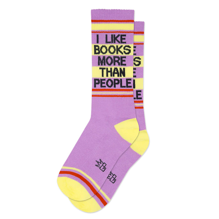 A pair of crew socks in lavender purple and yellow with red stripes, featuring the text 'I LIKE BOOKS MORE THAN PEOPLE' in black block letters, shown on a plain white background.