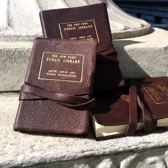 Three Italian leather journals with The New York Public Library gold stamp, tied with string, displayed on a stone surface.