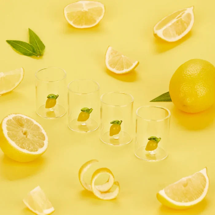 Clear glass cups with lemon designs on a yellow background with lemons and leaves.