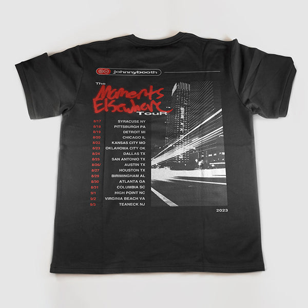 Black t-shirt with Johnny Booth branding, a cityscape at night with light streaks, red The Moments Elsewhere Tour text, and tour dates and cities listed.