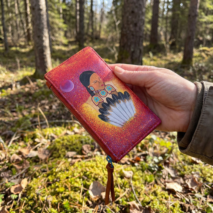 Hand holding a colorful wallet with a Native American design in a forest setting