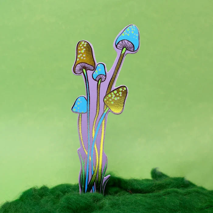 A lilac with blue and gold details bookmark shaped as a mushrooms against a solid light green background.