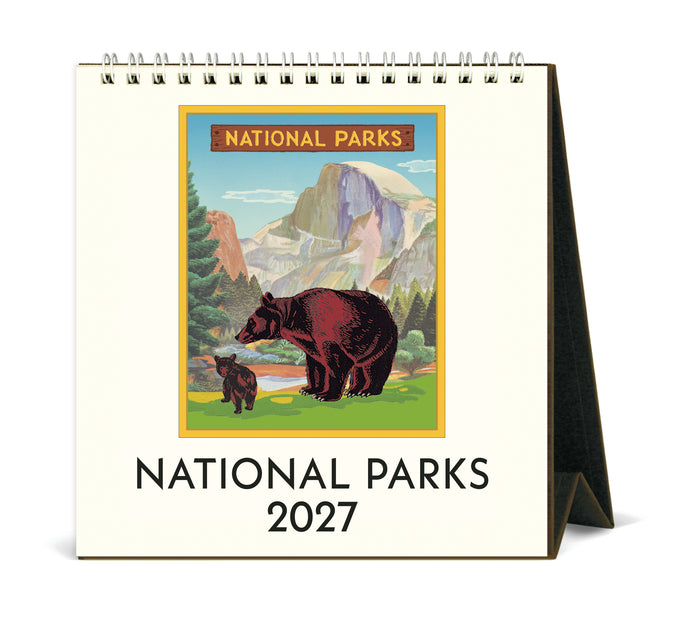 A spiral-bound 2027 National Parks desk calendar shown standing on its side. The front cover features an illustrated scene of a grizzly bear and a calf in a mountain landscape, with the text 'NATIONAL PARKS 2027' below.