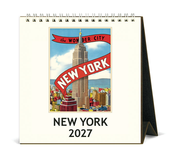 A spiral-bound 2027 New York desk calendar shown standing on its A-frame base. The front cover features a vintage-style travel poster of the New York City skyline with the Empire State Building, under a red banner reading 'the WONDER CITY' and 'NEW YORK'.