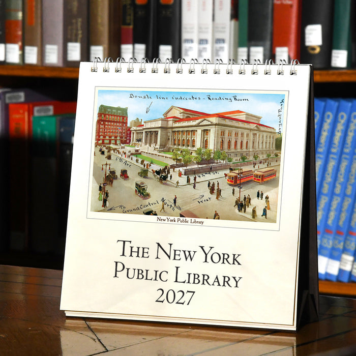 A spiral-bound 2027 desk calendar titled 'The New York Public Library 2027' standing on a wooden table in front of bookshelves. The calendar cover features a vintage illustration of the New York Public Library.