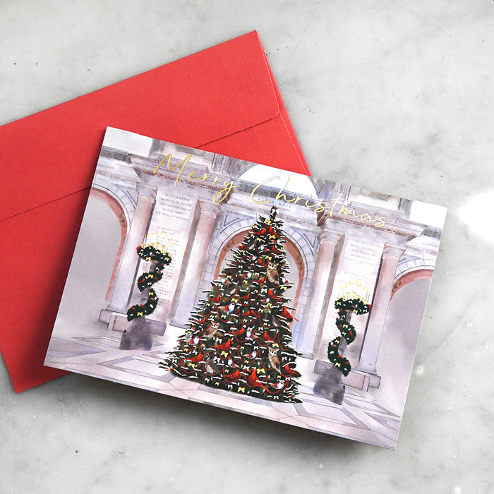 Christmas card with the Astor Hall decorated Christmas tree and red envelope on a light gray surface