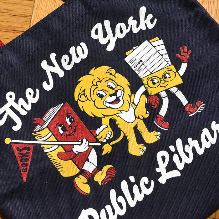 A close-up of a dark navy tote bag featuring a colorful graphic of cartoon books and a lion character with the text 'The New York Public Library' and 'BOOKS'.