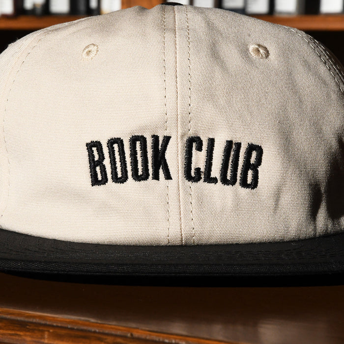 Beige cap with 'BOOK CLUB' text on a wooden surface