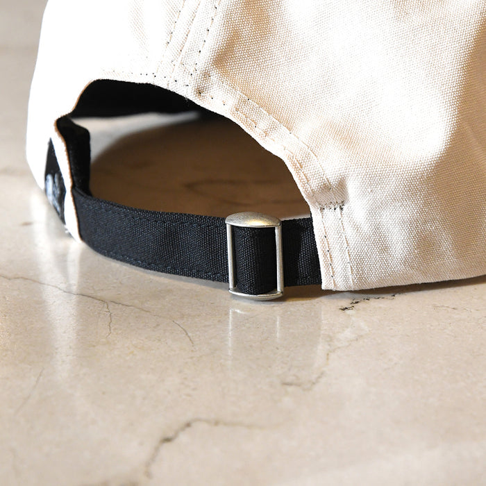 Close-up of a beige cap with a black strap and metal buckle on a marble surface