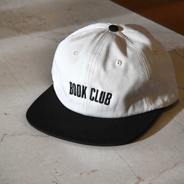 Off-white cap with black brim and 'BOOK CLUB' text .