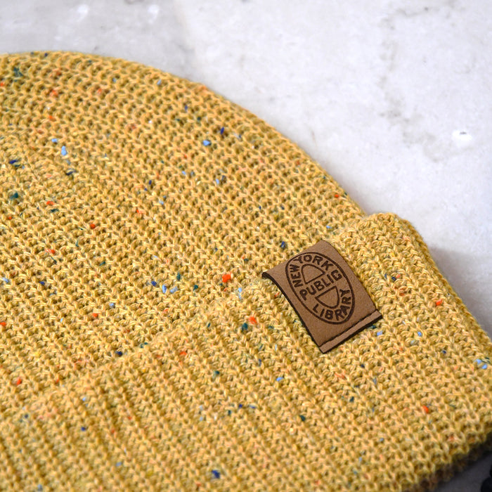 Close up of the brown leather patch of an oval NYPL stamp on a mustard beanie.