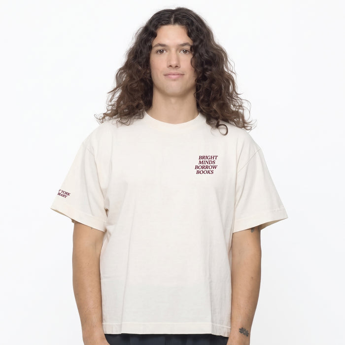 A man a cream-colored t-shirt with dark red text on the left chest that reads 'BRIGHT MINDS BORROW BOOKS'. The background is a clean white studio backdrop.