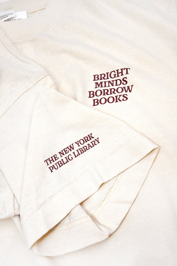 An off-white cotton t-shirt featuring dark red printed text on the chest reading 'BRIGHT MINDS BORROW BOOKS' and on the sleeve reading 'THE NEW YORK PUBLIC LIBRARY'.