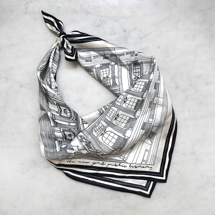 The squared off-white silk scarf tied in a triangular  style on a white marble surface.
