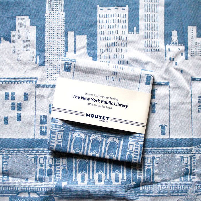 The tea towel with cityscape design and a folded fabric sample on top