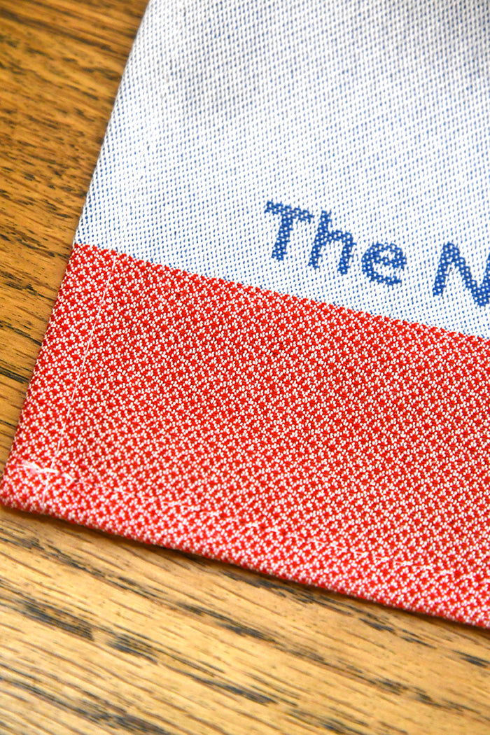 Close-up of a fabric edge with red pattern and off-blue label on a wooden surface