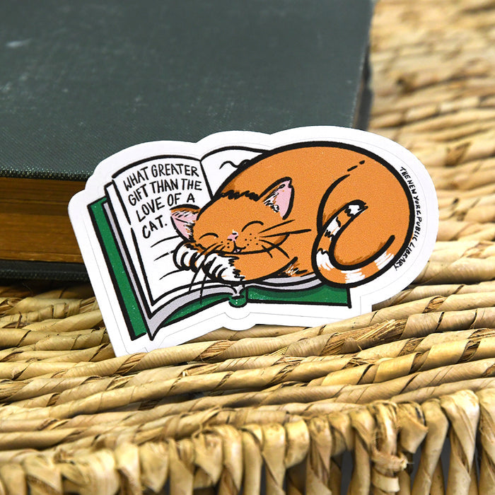 Sticker shows illustration of an orange cat sitting on top of a green open book. Text on book reads: What greater gift than the love of a cat.