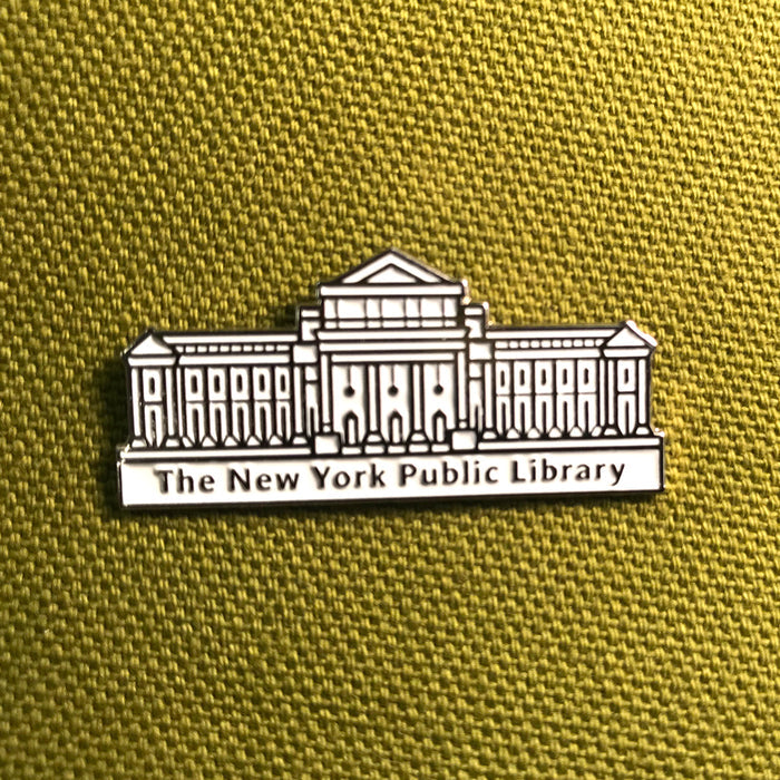 An enamel pin depicting the New York Public Library building in white and black, placed on a yellow textured background.