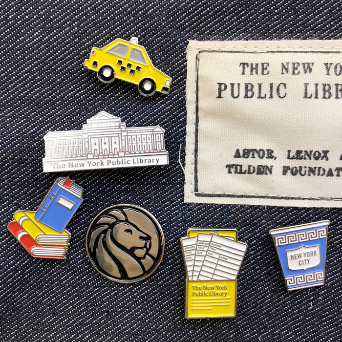 Photo shows different enamel pins related to NYPL and New York City.