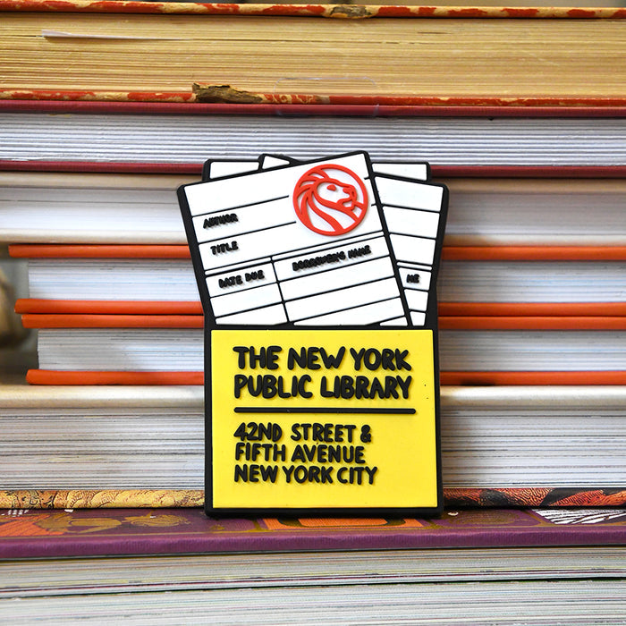 Rubber magnet simulating a NYPL library card. Text on yellow pouch reads: The New York Public Library. 42nd street & Fifth Avenue New York City.