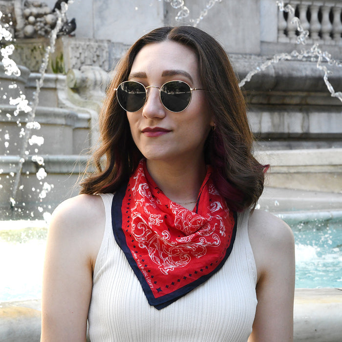 Woman wearing a red bandana with a navy blue border and white patterns in front of a fountain. Text on bandana reads: The New York Public Library.
