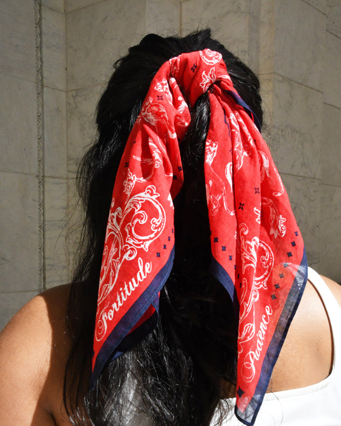 Person wearing a red bandana with white patterns and text on their head, against a beige wall. Corners of the bandana read: Patience. Fortitude.
