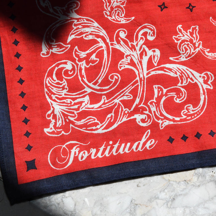 Red bandana with navy blue border featuring white floral design and 'Fortitude' text on a marble surface