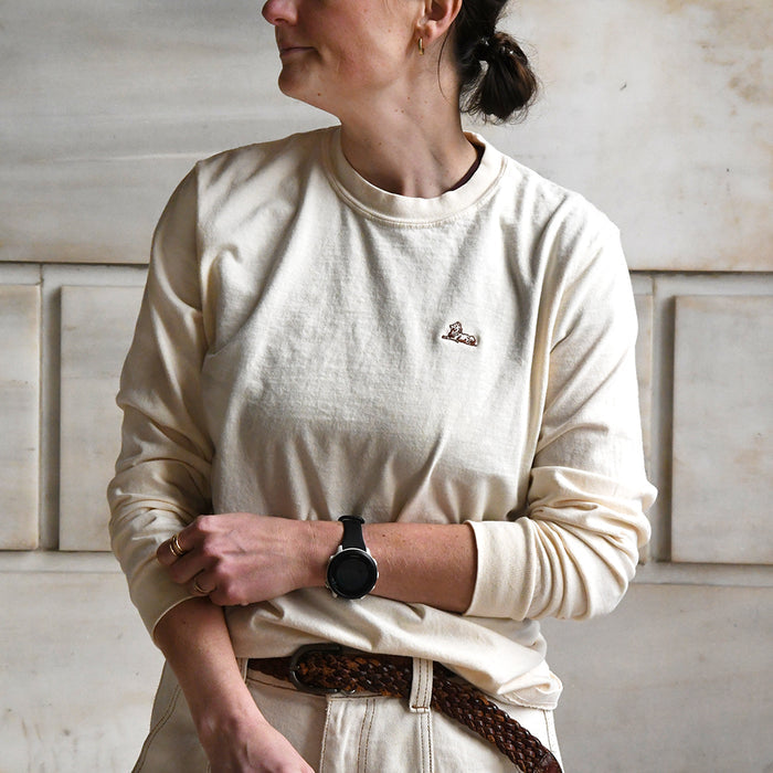 Person wearing a cream-colored long sleeve t-shirt with an embroidered illustration of one of the NYPL lions in the left side of the chest area.