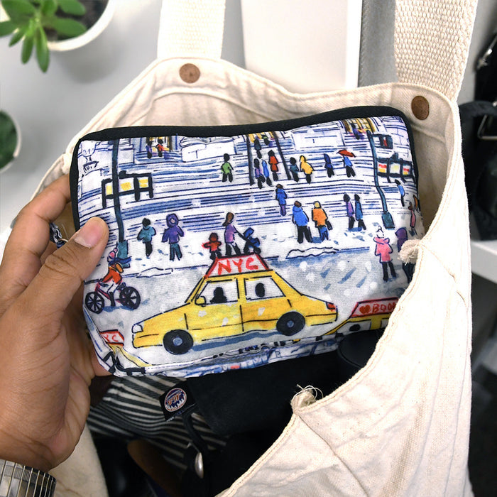 Hand holding a small pouch with a colorful design of a yellow taxi and people on a street.