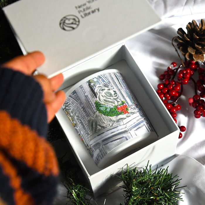 A person opening the box of the candle with a festive NYPL lion illustration.