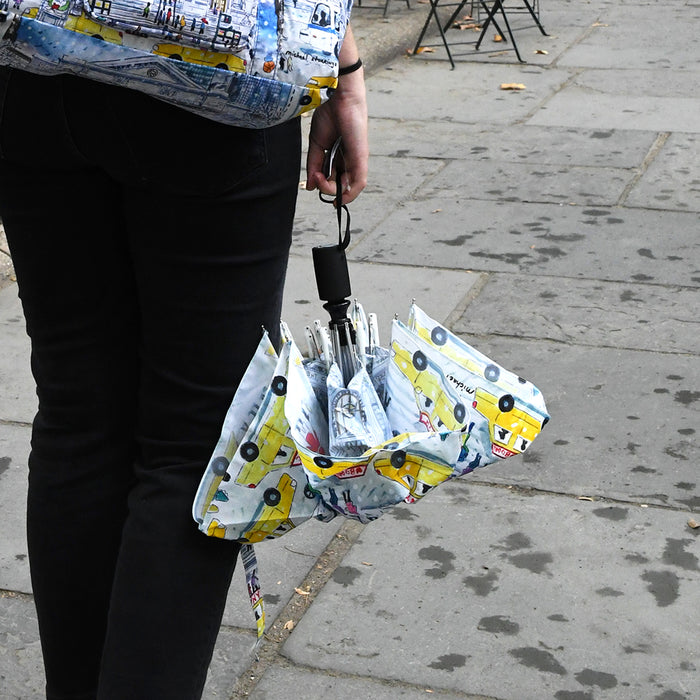 Person holding a folded umbrella where you can see the taxi cabs in the illustration.