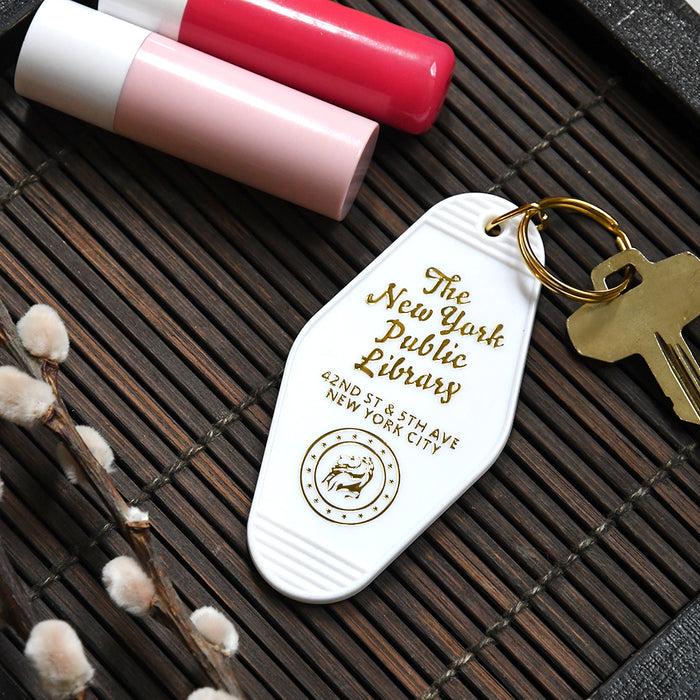 A white, diamond-shaped vintage motel-style keychain resting on a dark bamboo mat.
