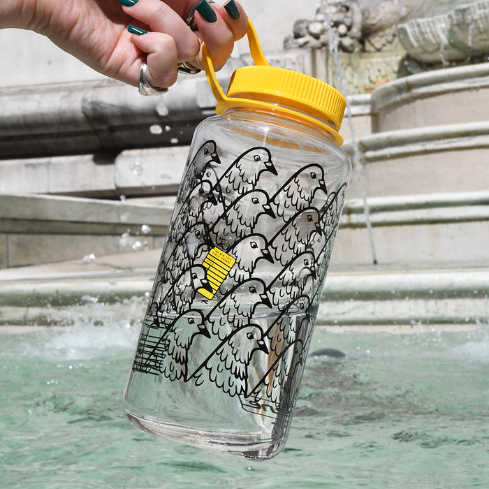 Clear water bottle with pigeon design and yellow cap held over a fountain