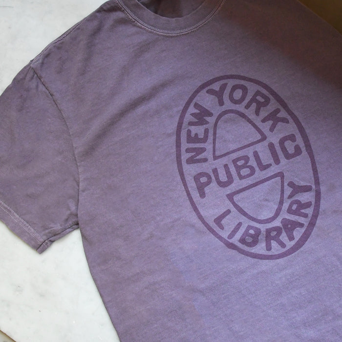Close-up of purple shirt that features an oval NYPL bookbinding stamp.